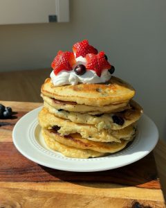 Brown Butter Blueberry Sourdough Pancakes stacked on plate with whipped cream and berries