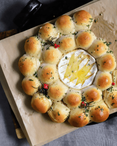 baked brie wreath with garlic parker house rolls resting on a pizza stone. golden and glossy from the garlic butter and baking.