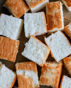 Cubed angel food cake cut into even pieces, prepared for use in a layered dessert such as a trifle, showing its light, airy texture and soft crumb.