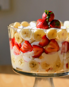 A trifle filled with cake, vanilla pudding, fresh slices of bananas and homemade strawberry preserves, topped with whipped cream and fresh strawberries.