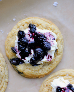 Blueberry cornbread cookies topped with swirls of whipped salted honey buttercream and garnished with blueberry compote.