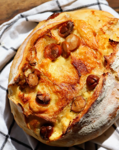 Golden cheesy hot dog focaccia loaf resting on a kitchen towel, with melted cheese and pieces of hot dog baked into the crust.