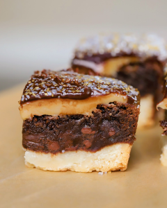Close-up of a millionaire brownie slice showing distinct layers of buttery shortbread, rich brownie, smooth caramel, and glossy chocolate.
