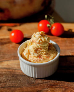 A porcelain bowl filled with creamy roasted tomato butter sits in warm sunlight, with fresh cherry tomatoes softly blurred in the background, creating a bright and rustic kitchen scene.