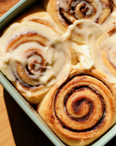 Soft, fluffy cinnamon rolls baked together in a pan and topped with brown butter cream cheese frosting, which is slowly melting over the warm rolls