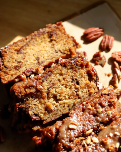Sliced sticky pecan cinnamon swirl banana bread with a gooey maple pecan topping, showcasing the swirls of cinnamon sugar throughout the moist loaf, illuminated by warm golden sunlight.
