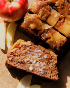 A golden loaf of upside down caramelized apple bread topped with tender caramelized apple slices and chopped pecans, served on a plate, topped with butter and flaky sea salt.