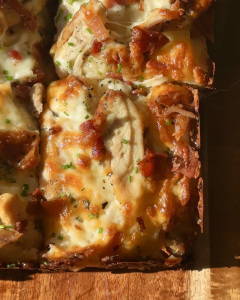 sliced focaccia on a cutting board with melty cheese, sliced chicken and bacon bits.