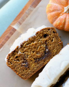 slice of the cinnamon roll pumpkin bread exposing the cinnamon swirl with the brown butter cream cheese frosting on top.