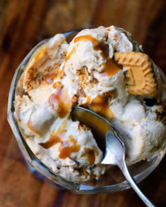 scooped biscoff and salted caramel ice cream in a large glass bowl with a spoon going in for a scoop